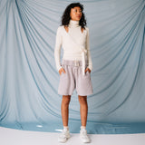 A model wears a white fuzzy sweater and the pale lavender stone Yacht Shorts by Les Tien against a soft blue backdrop - full outfit view.