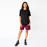 A model wears the merlot-red pigment dyed Yacht sweat shorts by Les Tien, paired with a black t-shirt and black loafers - full outfit view.