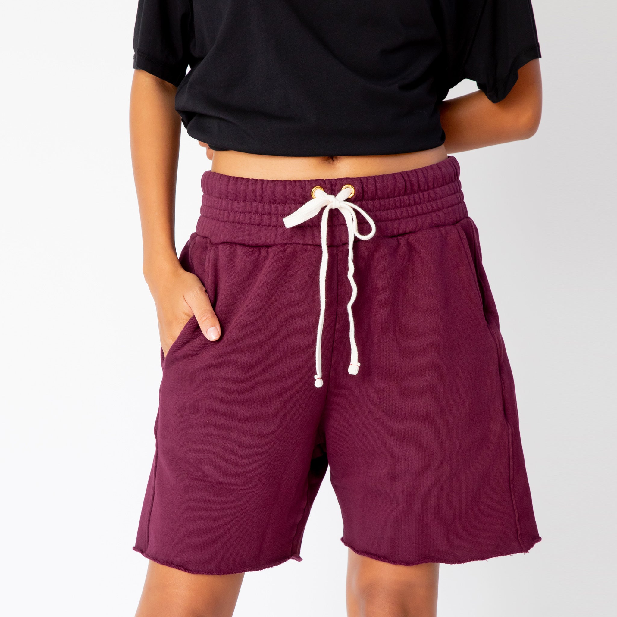 A model wears the merlot-red pigment dyed Yacht sweat shorts by Les Tien, paired with a black t-shirt - front detailed view of white drawstrings and wide elastic waist band.