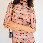 A model wears the graphic pleated Rainer dress in the pink Wallace color way, detailed view.