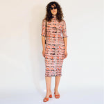 A model wears the graphic pleated Rainer dress in the pink Wallace color way, front view.