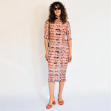 A model wears the graphic pleated Rainer dress in the pink Wallace color way, front view.