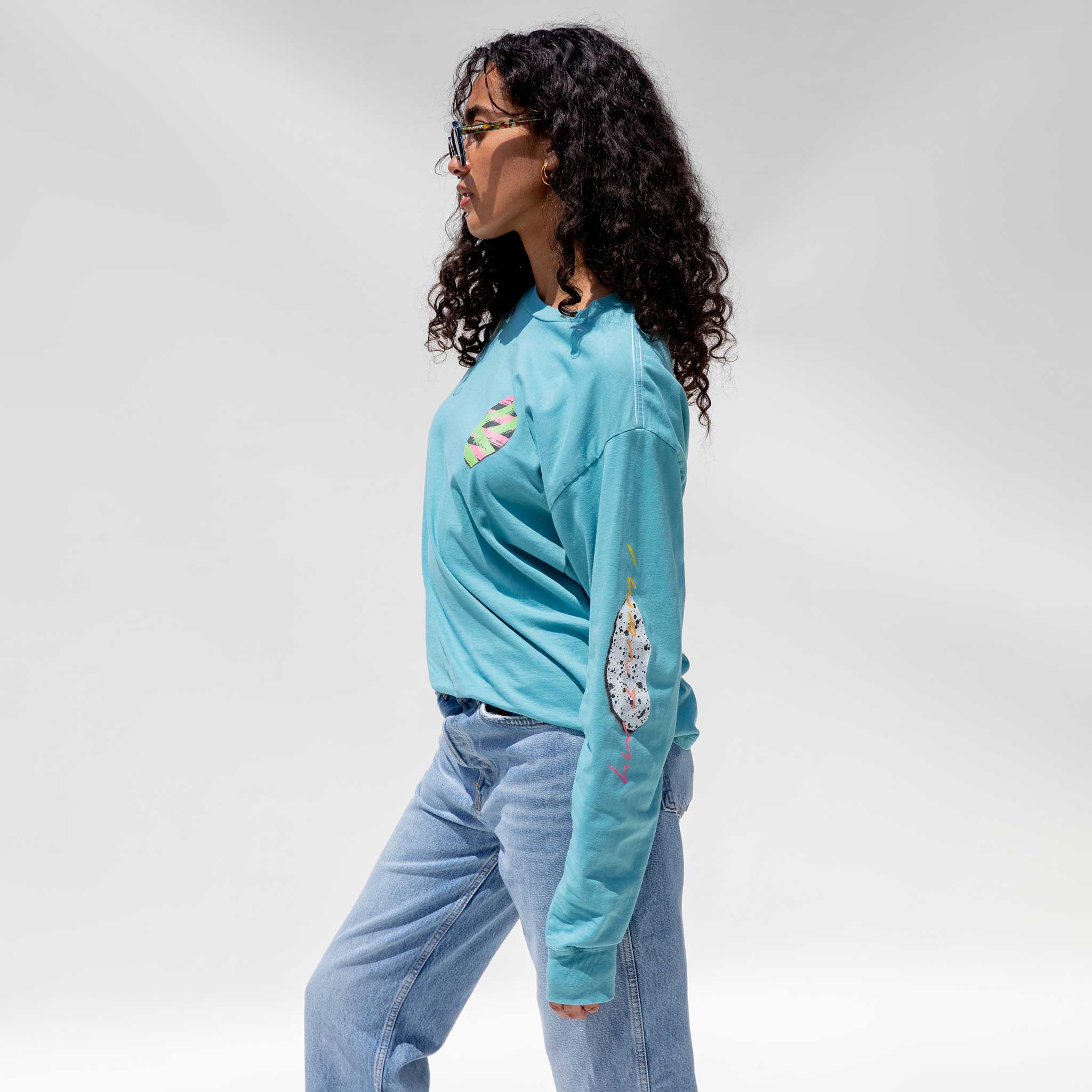 Side detail photo of model wearing the Vintage Washed LCD10 Long Sleeve Graphic Tee - Teal. 