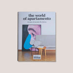 Photo of book cover for The World of Apartamento, showing a large Baldessari print leaned against a living room wall with a white sofa and parquet floors.