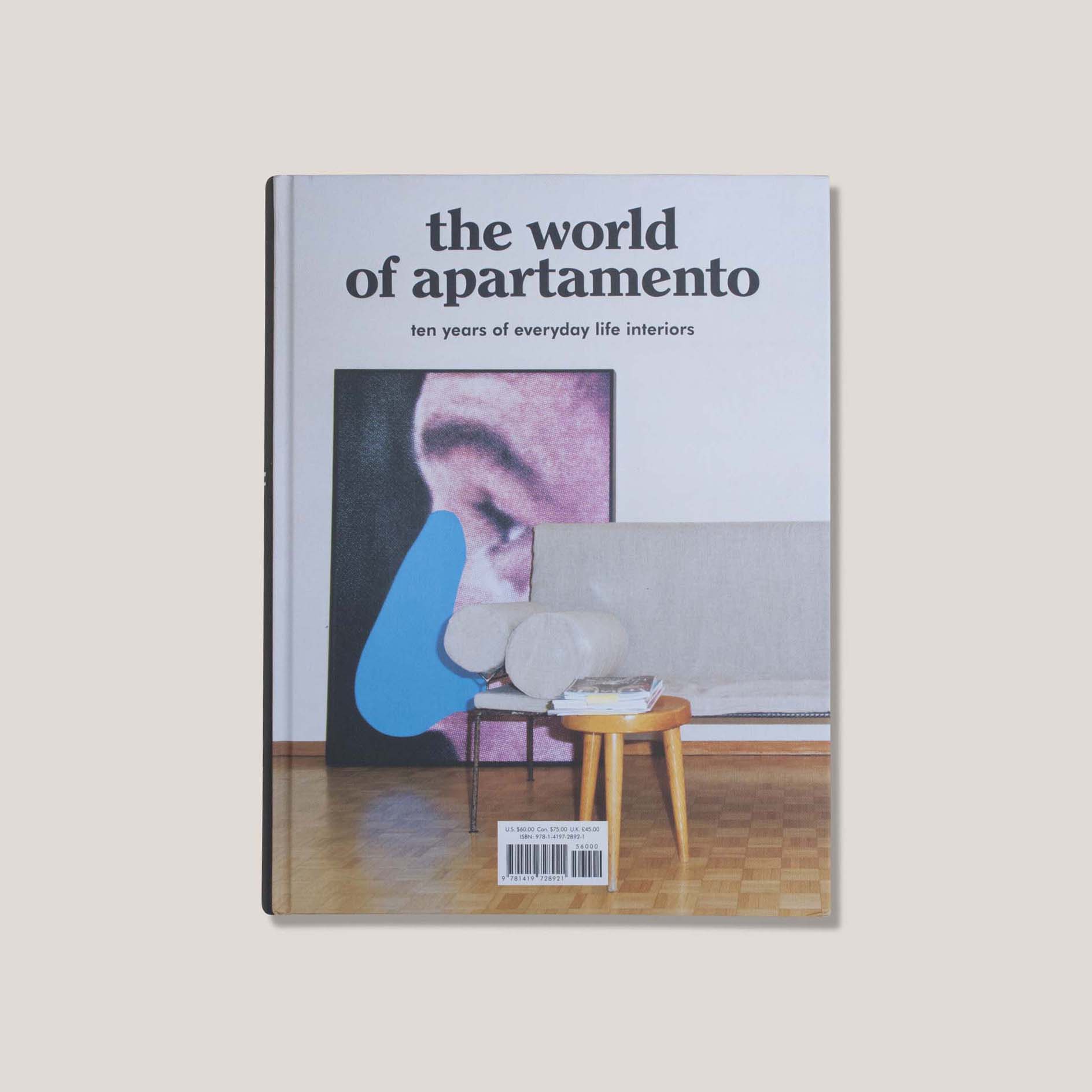 Photo of book cover for The World of Apartamento, showing a large Baldessari print leaned against a living room wall with a white sofa and parquet floors.