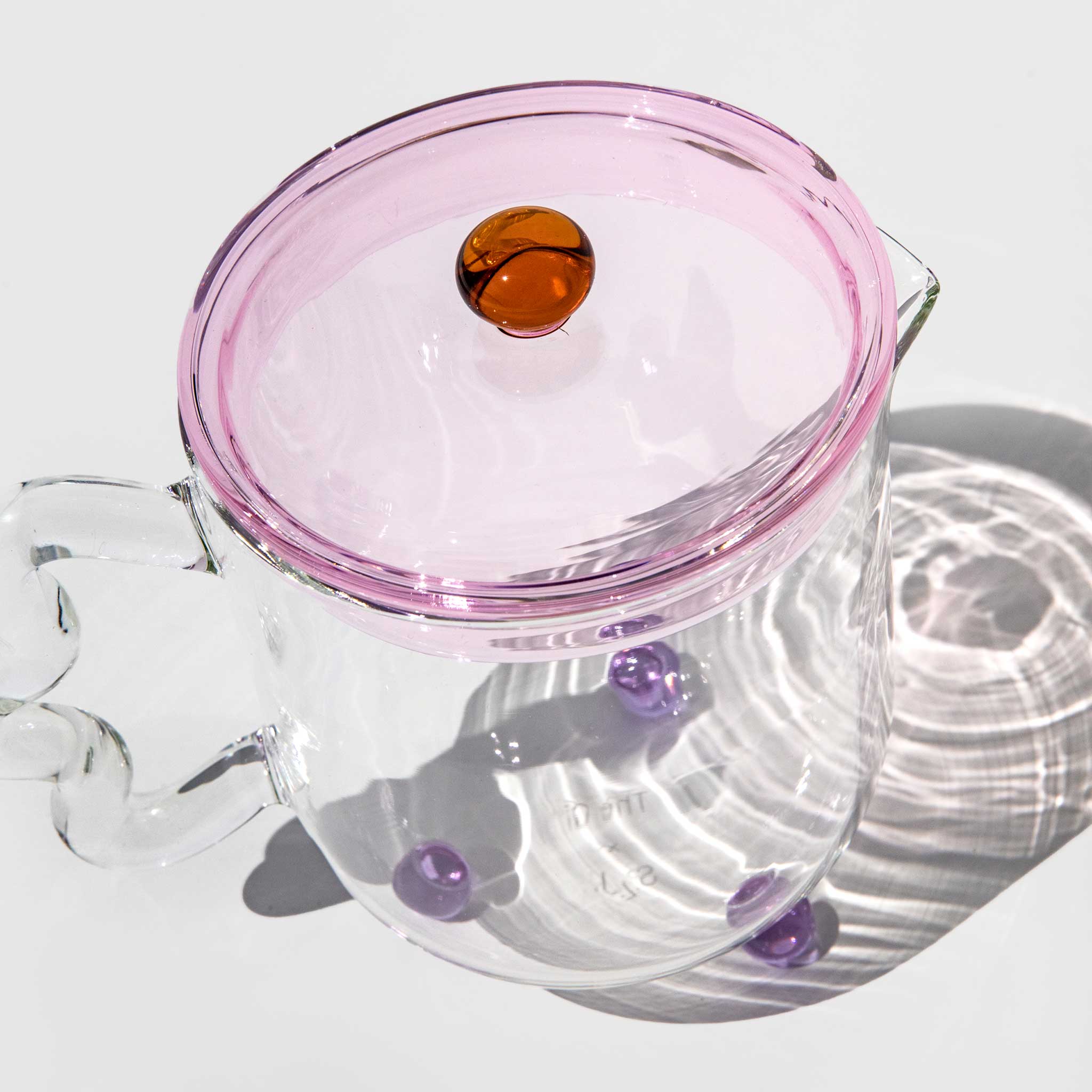 Elegant photo of the Bloom Teapot with a transparent pink tinted lid, clear base, and light wavy glass handle.