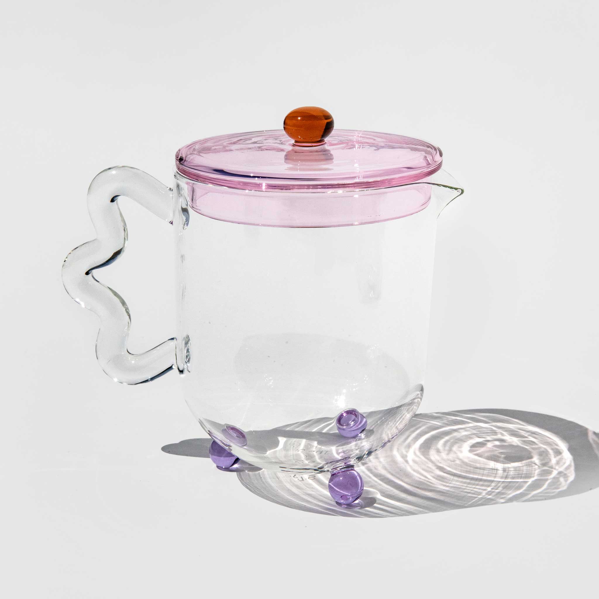 Elegant photo of the Bloom Teapot with a transparent pink tinted lid, clear base, and wavy glass handle.