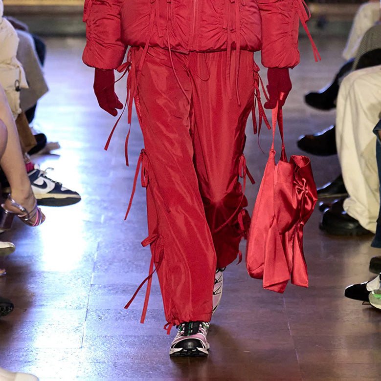 Runway photo of model wearing the Cam Pants - Red. The pants feature bows details down the side. 