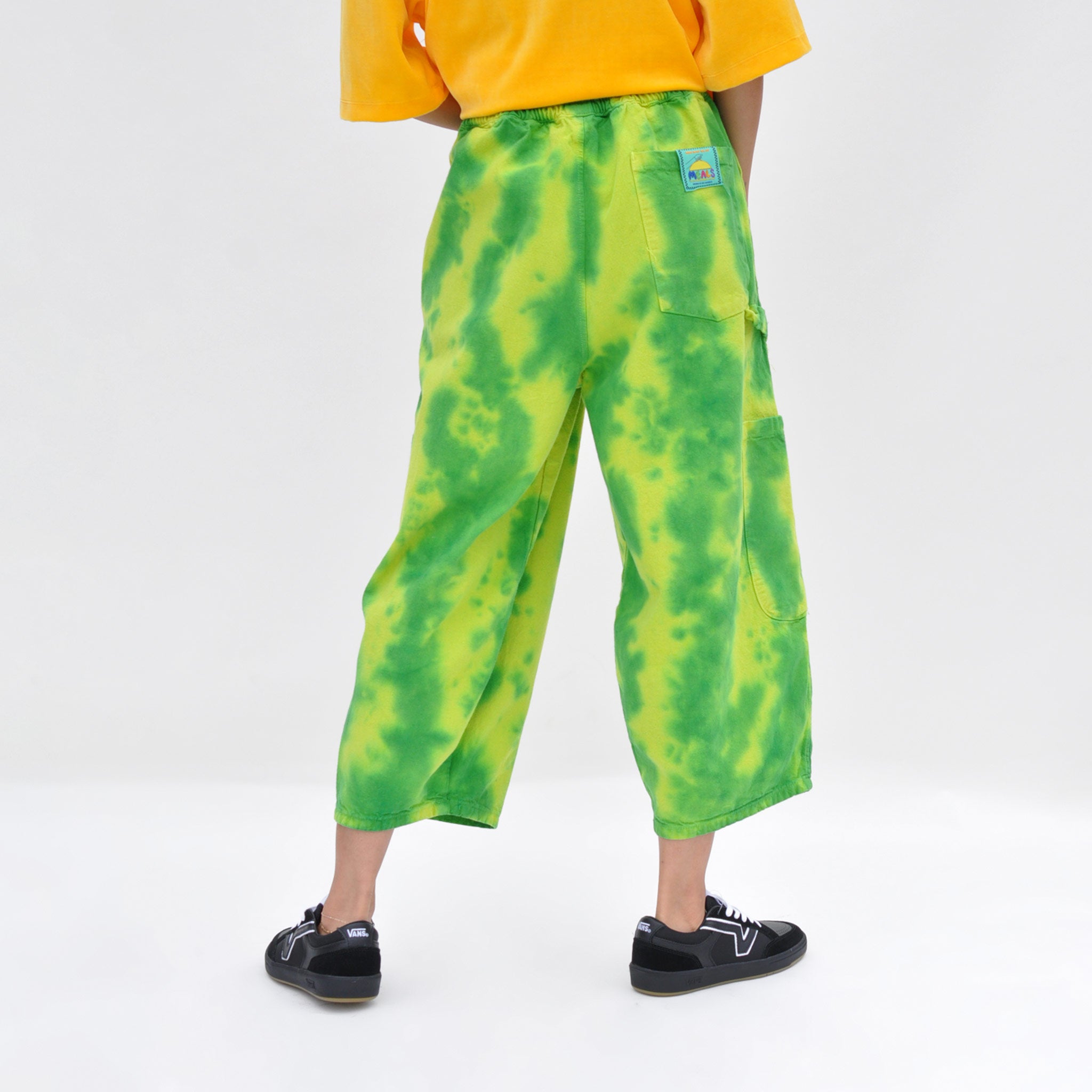 Back image of a model wearing the chef pants by meals in watermelon. these oversized Cargo pants are green and yellow tie-dye. Like the outside of a watermelon.