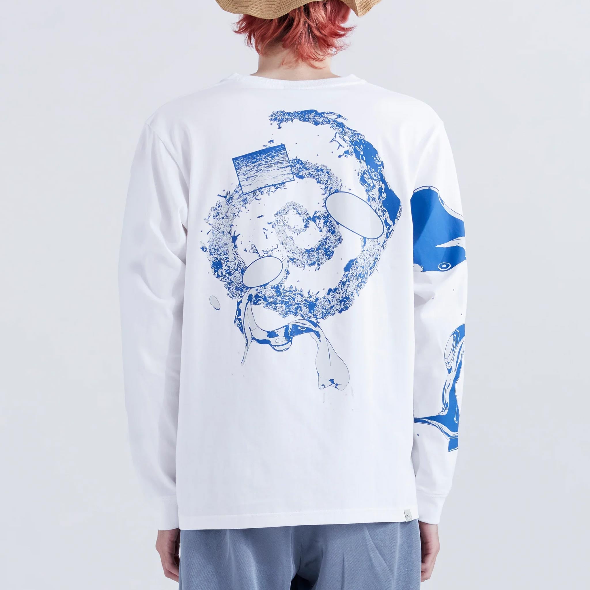 A model wears a white longsleeve cotton graphic tee with a blue spiral liquid graphic printed on the back and on the right sleeve.