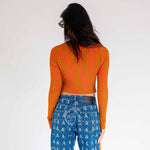 Back view of a model wearing the orange fluted sweater by Eckhaus Latta with hanging side tails.