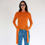 Half body photo of a model wearing the orange fluted sweater by Eckhaus Latta with hanging side tails.