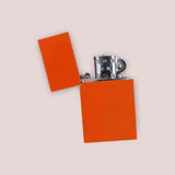 An orange rectangular lighter flipped open to reveal its flint mechanism.