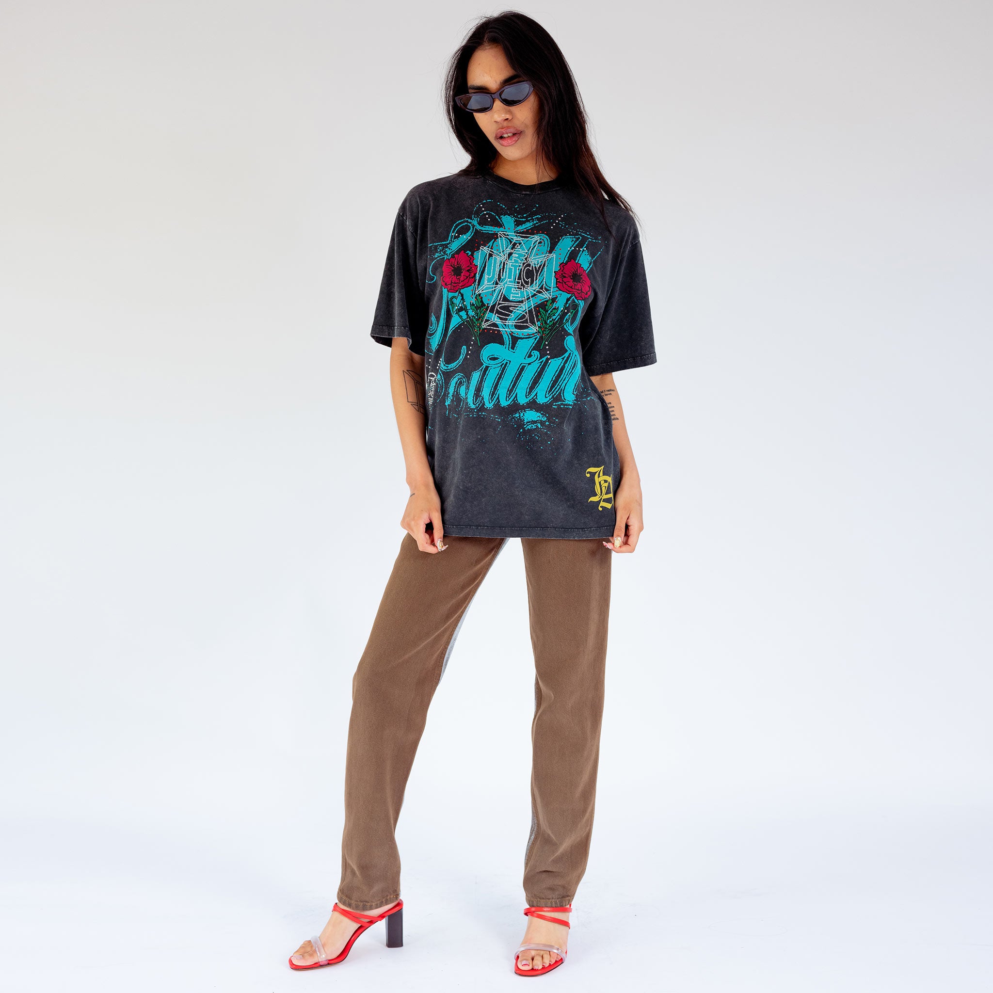 Full outfit view of a model wearing the faded black Juicy Loaded graphic tee with blue graphic lettering and rhinestone embellishments.