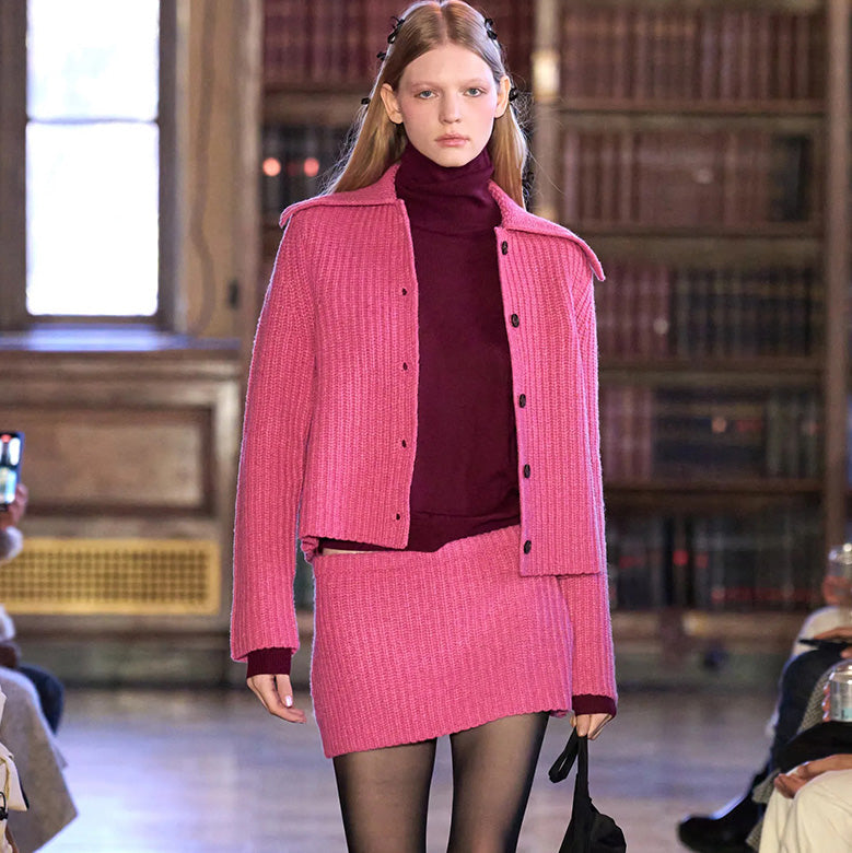 Runway photo of model wearing a knit pink set with a maroon turtleneck underneath. 