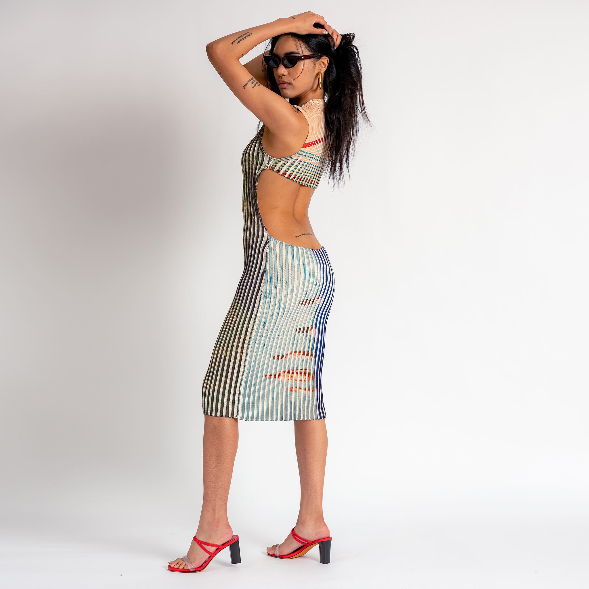 A model shows the back cutout of the sleeveless printed ribbed Ribboned Dress by Eckhaus Latta, which falls below the knee.