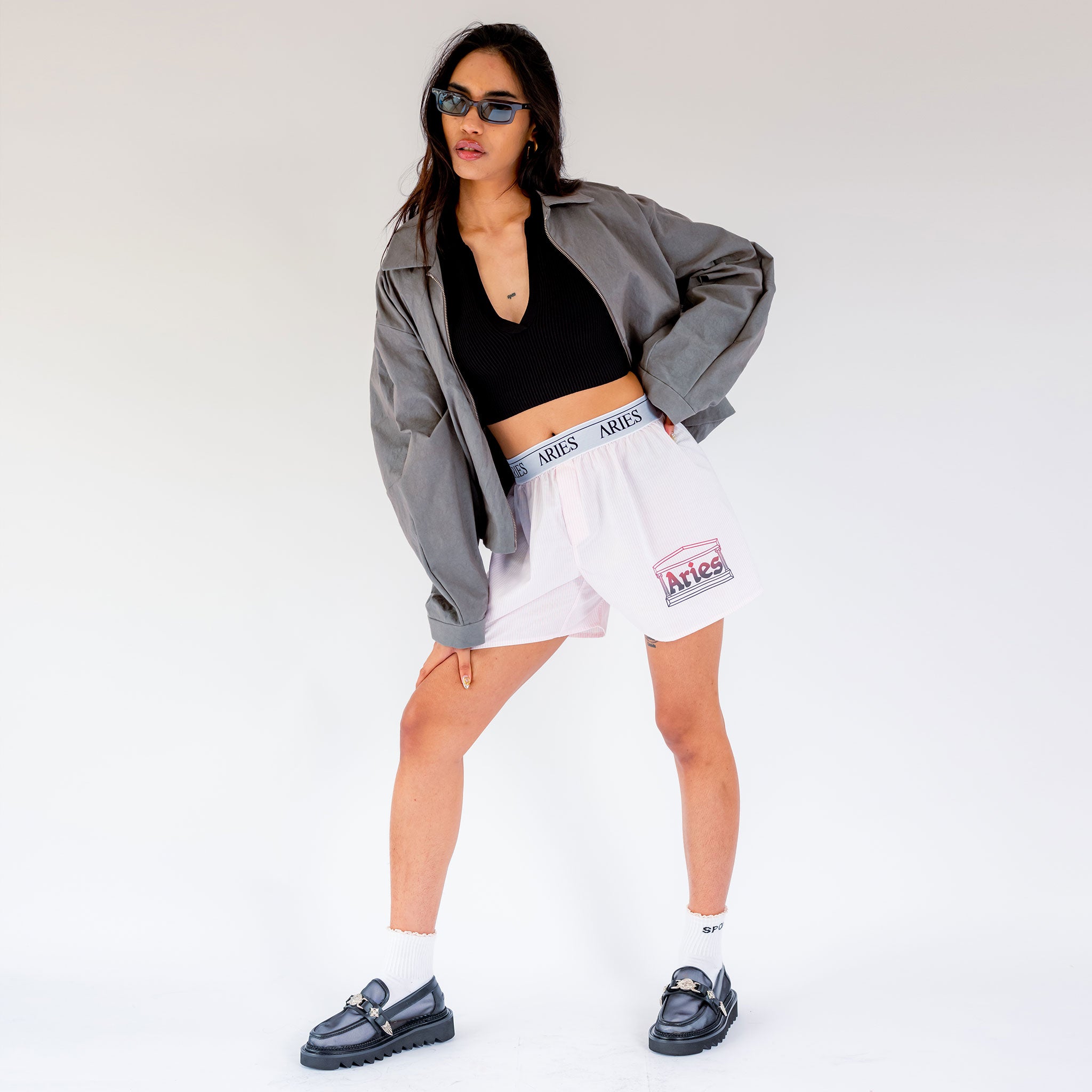 A model wears the unisex Aries Temple Boxing shorts with a logo printed waistband and pinstripes.