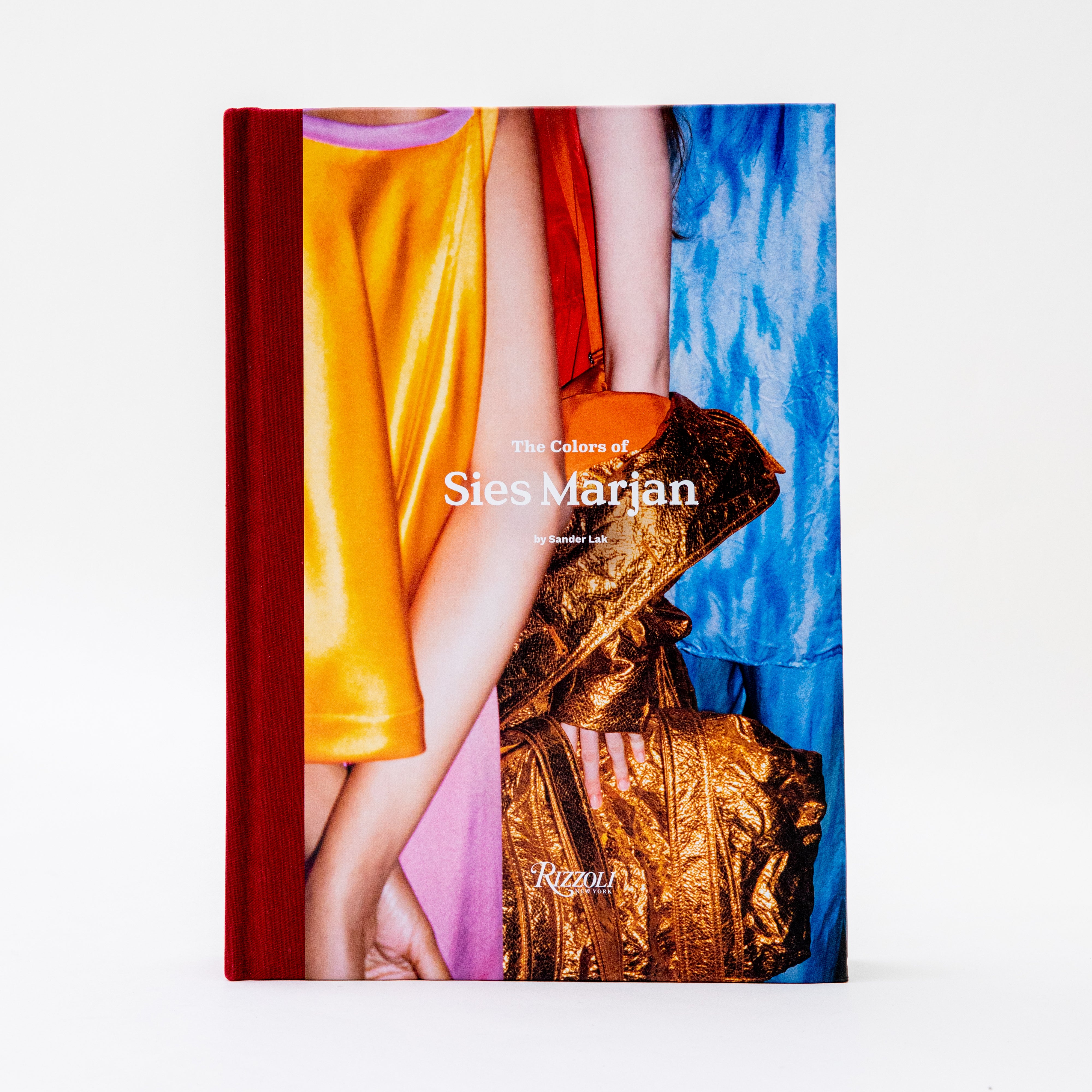 Sander Lak's The Colors of Sies Marjan, book cover image featuring a red binding, and a partial photograph of a model wearing a yellow satin skirt and carrying a metallic gold jacket and bag.