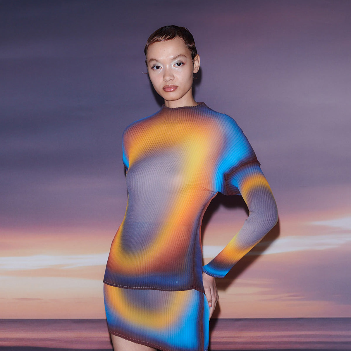 Close half body photo of model wearing the Tortas Top - Rain. The model is placed in front of a sunset background. 