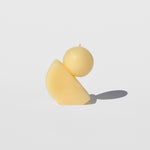 Photo of a small beeswax candle with a half moon shape base tilted at an angle with a spherical ball perched jauntily on top.
