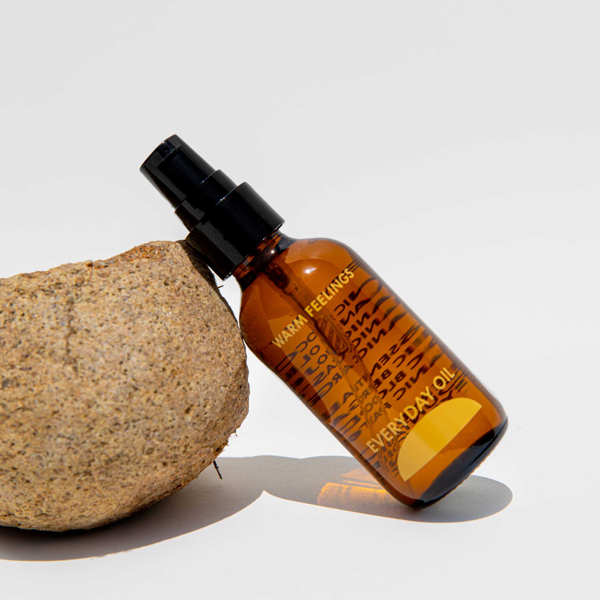 Close detail photo of the Everyday oil warm feelings oil on a white background next to a rock