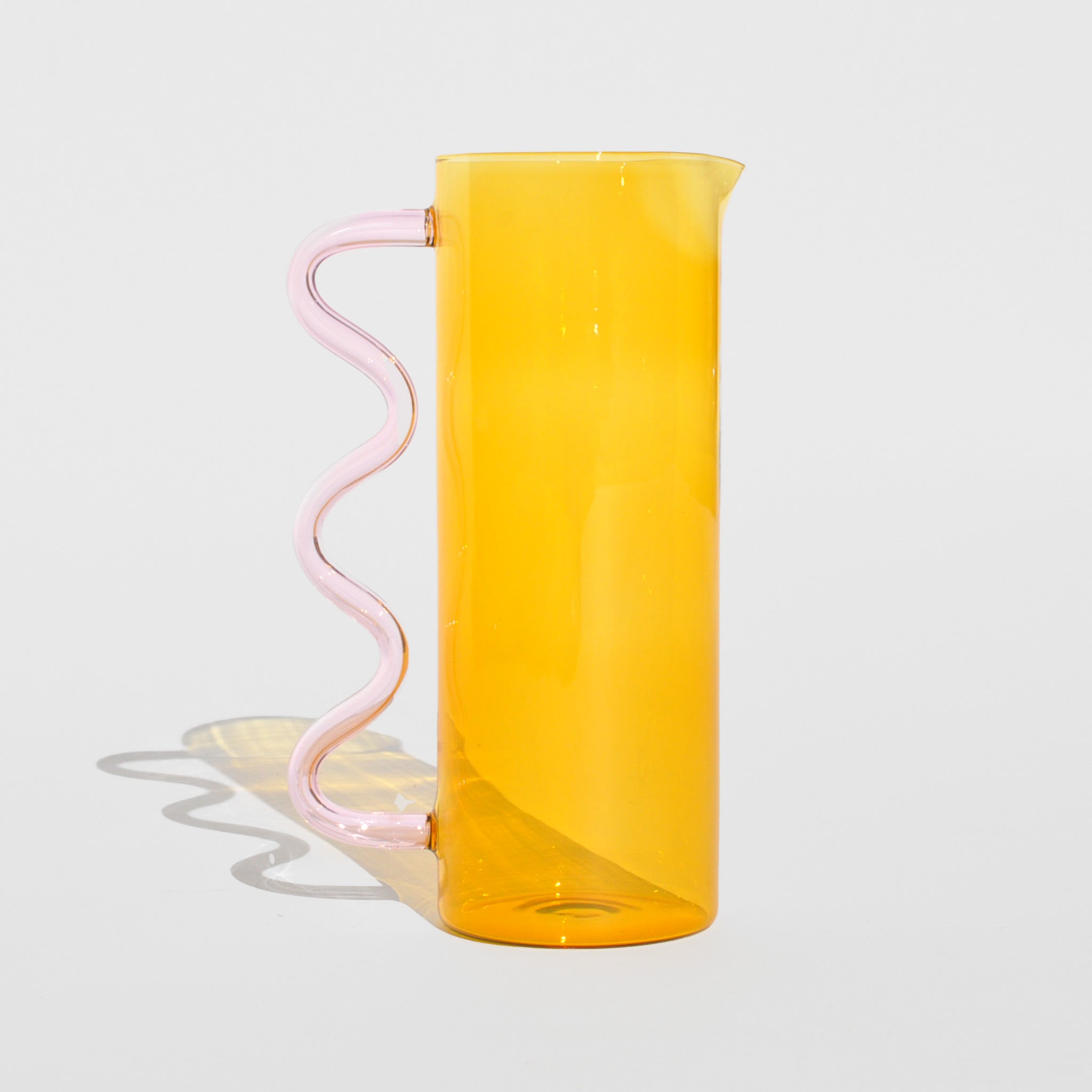 Photo of the Wave Pitcher - Yellow/Pink, a tall glass pitcher with a yellow cylindrical tank and a pink wavy glass handle.
