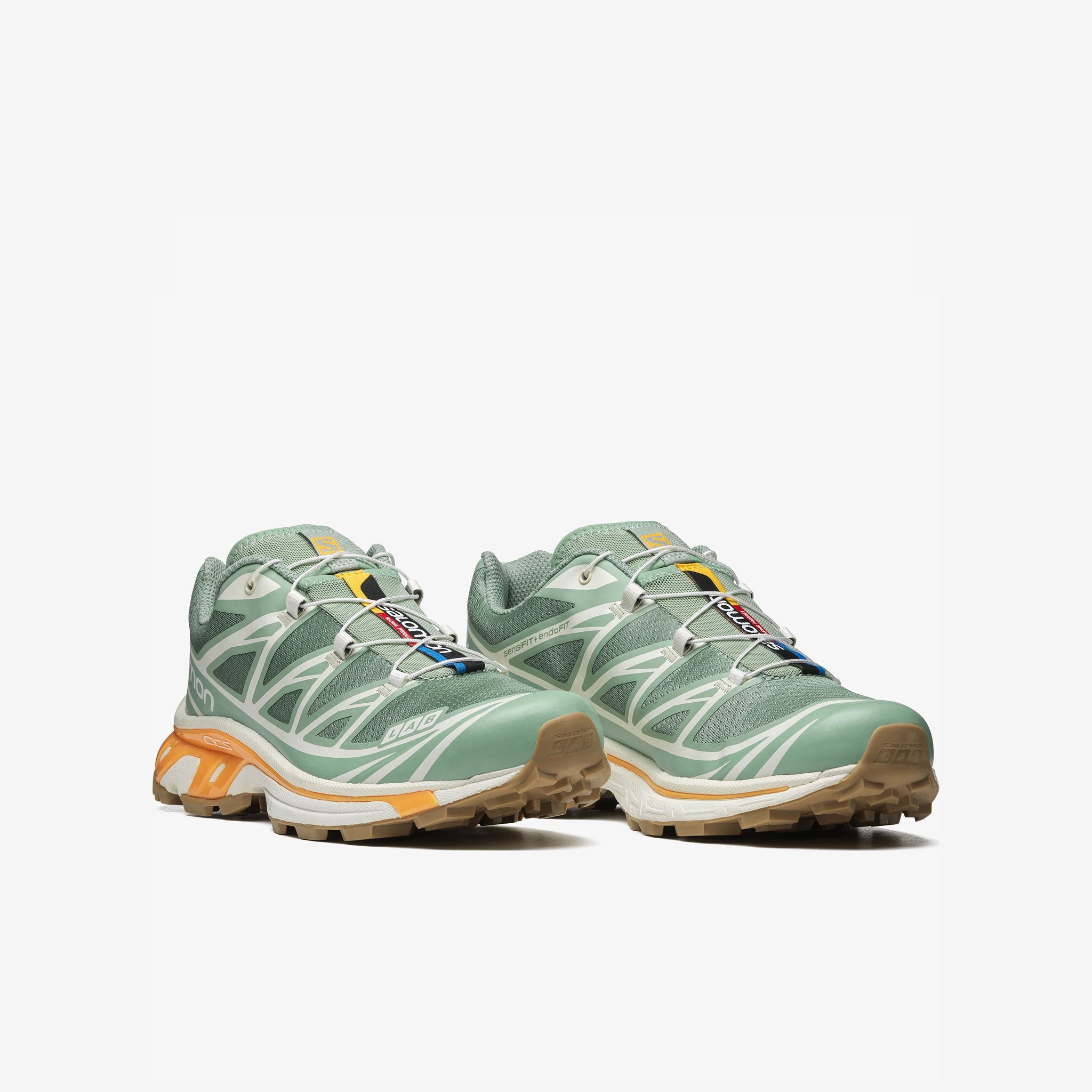 Salomon XT-6 sneakers in a pale green colorway with light orange trim along the sole. Angled front view.