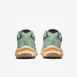 Salomon XT-6 sneakers in a pale green colorway with light orange trim along the sole. Back view.