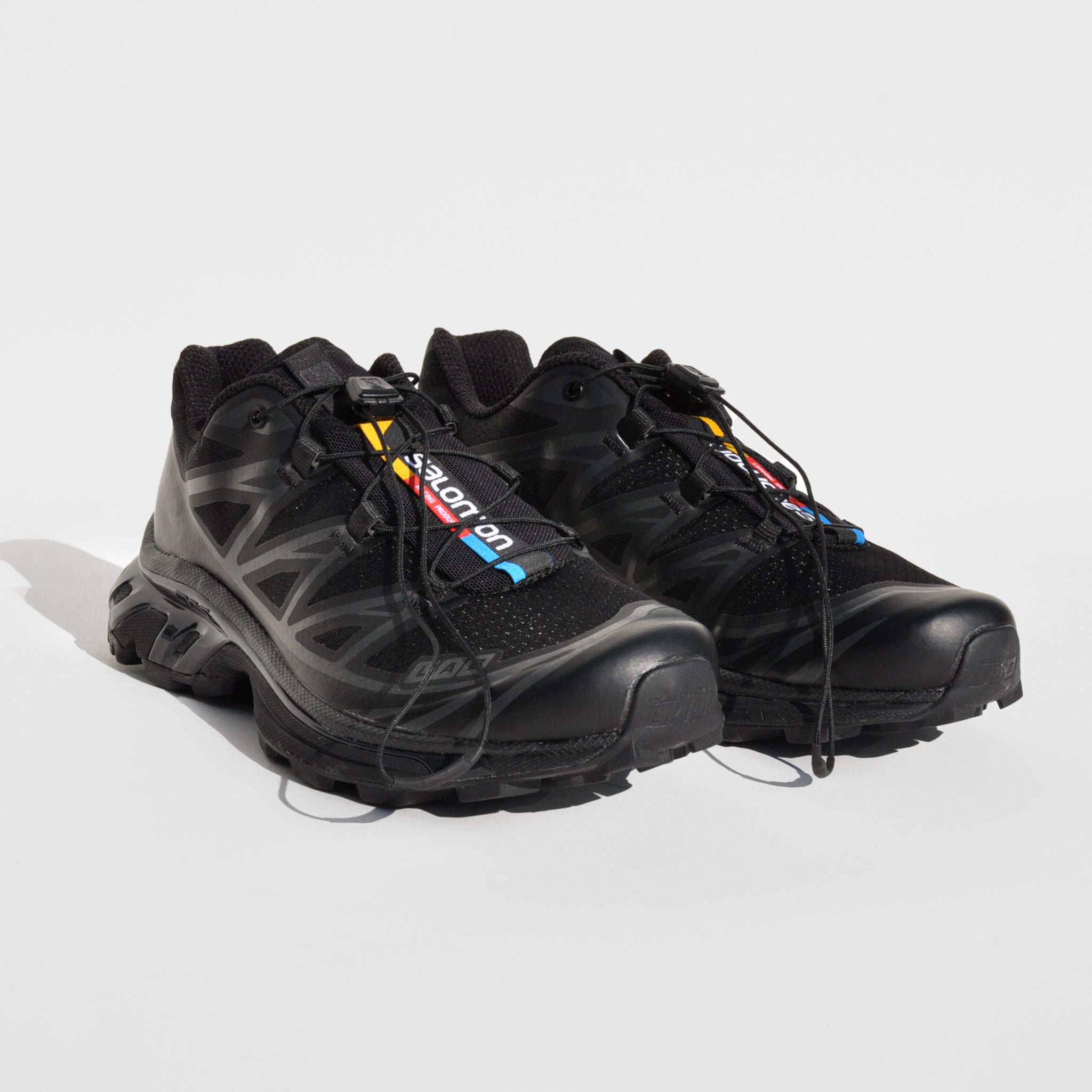 Front image of the XT-6-black sneakers by Salmon sport style in black. These sneakers are black with their rainbow logo down the middle tongue.