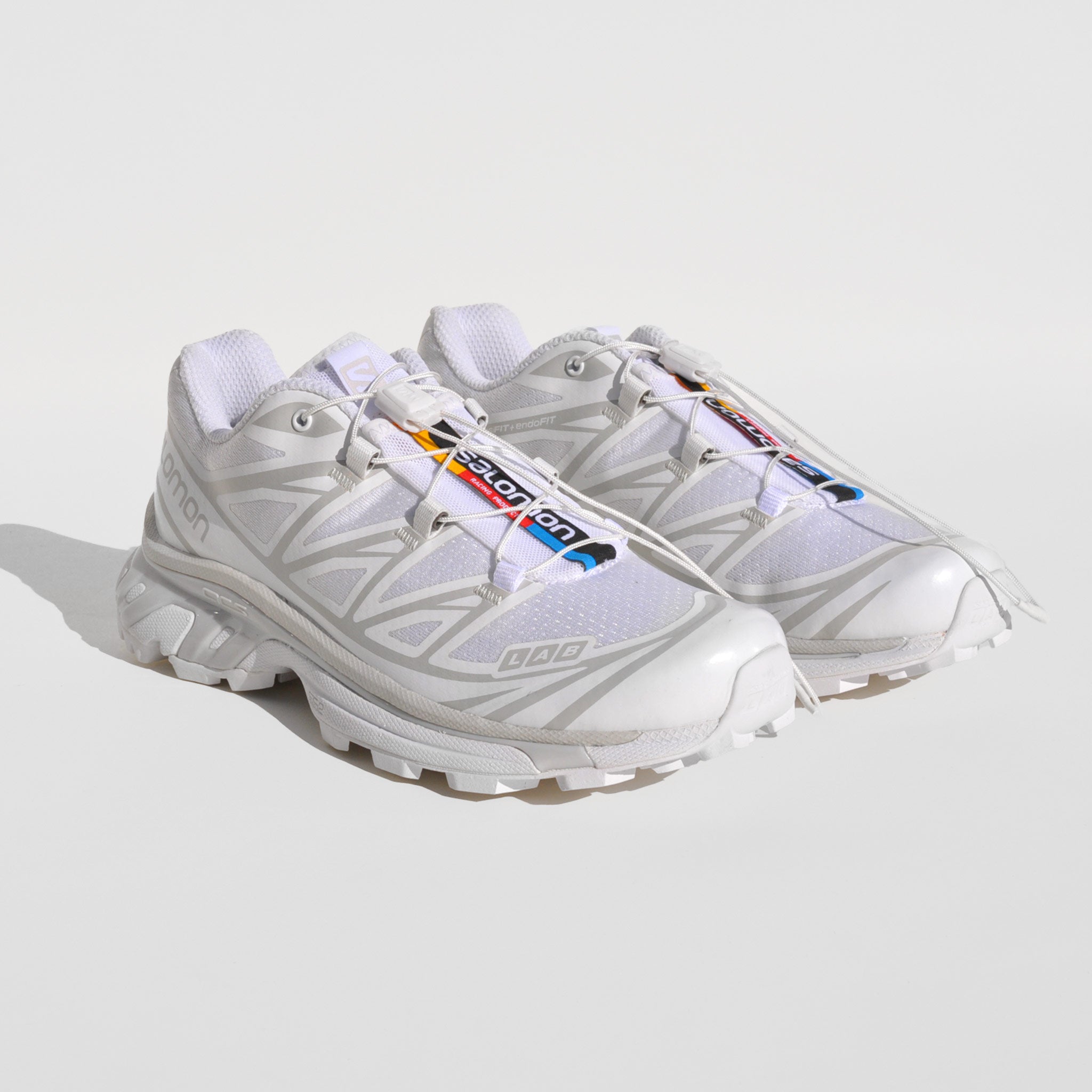 Front image of the XT-6-white sneakers by Salmon sport style in white. These sneakers are white with their rainbow logo down the middle tongue.